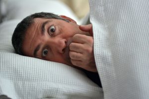 Mann fürchtet sich und versteckt sich unter der Bettdecke